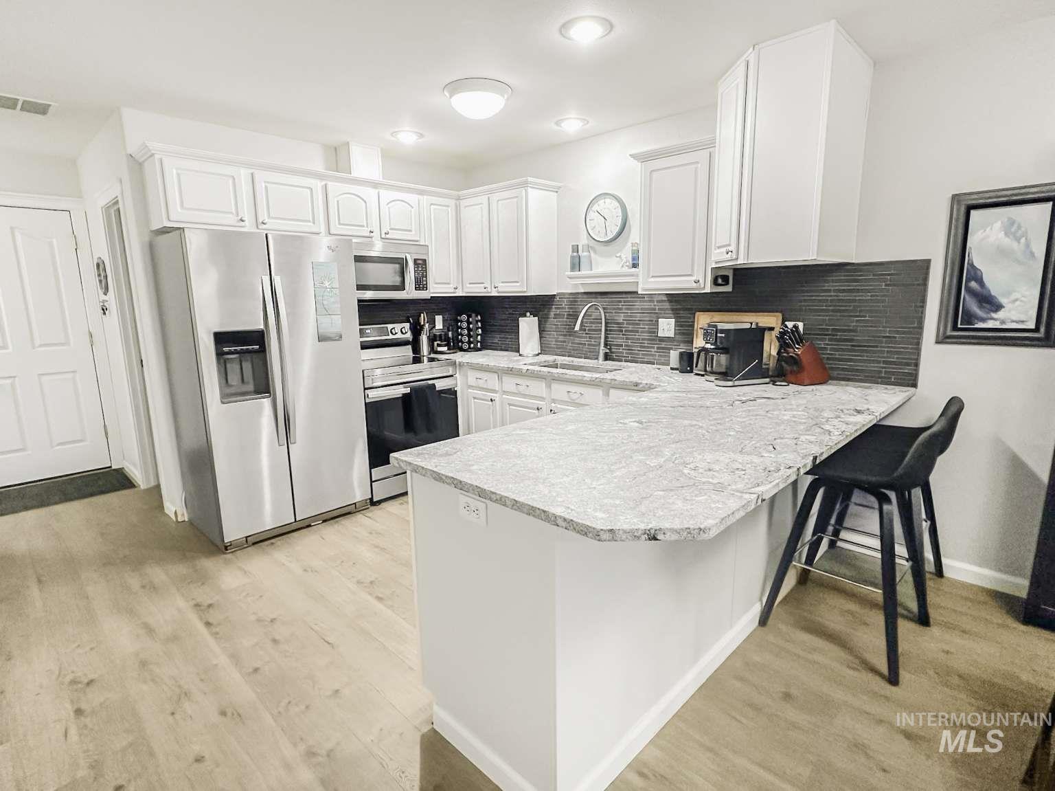 Kitchen featuring stainless steel appliances, light countertops, tasteful backsplash, and white cabinetry