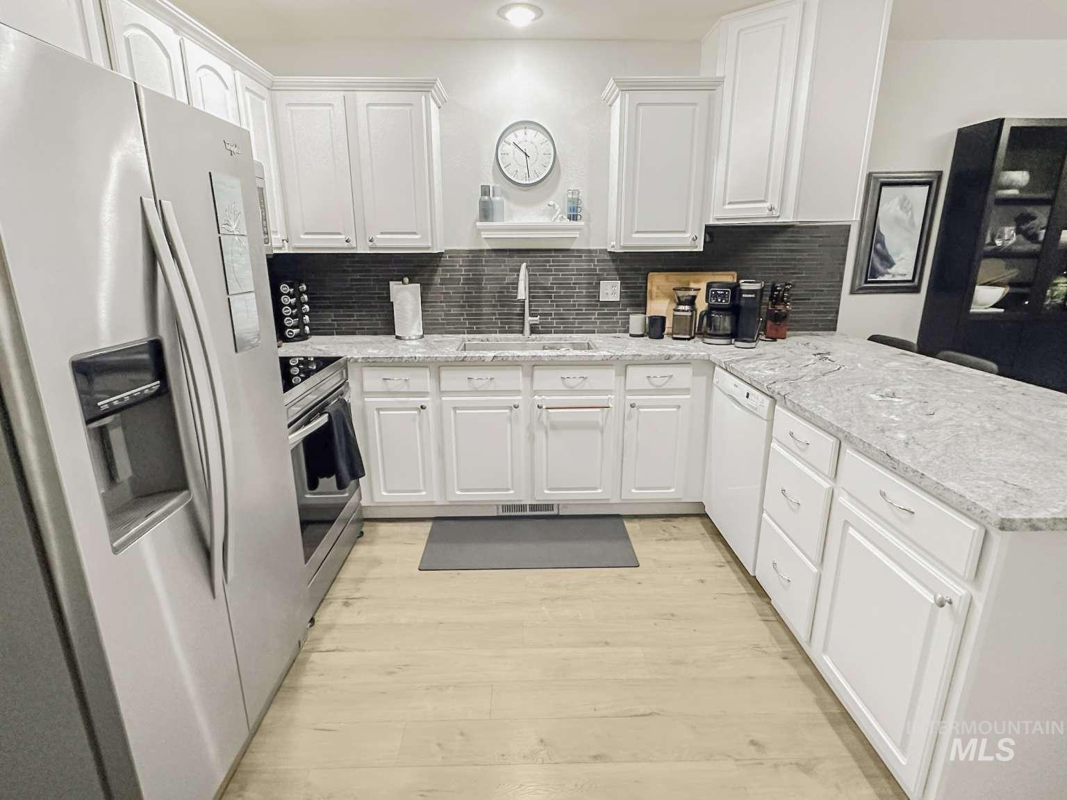 Kitchen featuring appliances with stainless steel finishes, a peninsula, white cabinets, light wood finished floors, and decorative backsplash