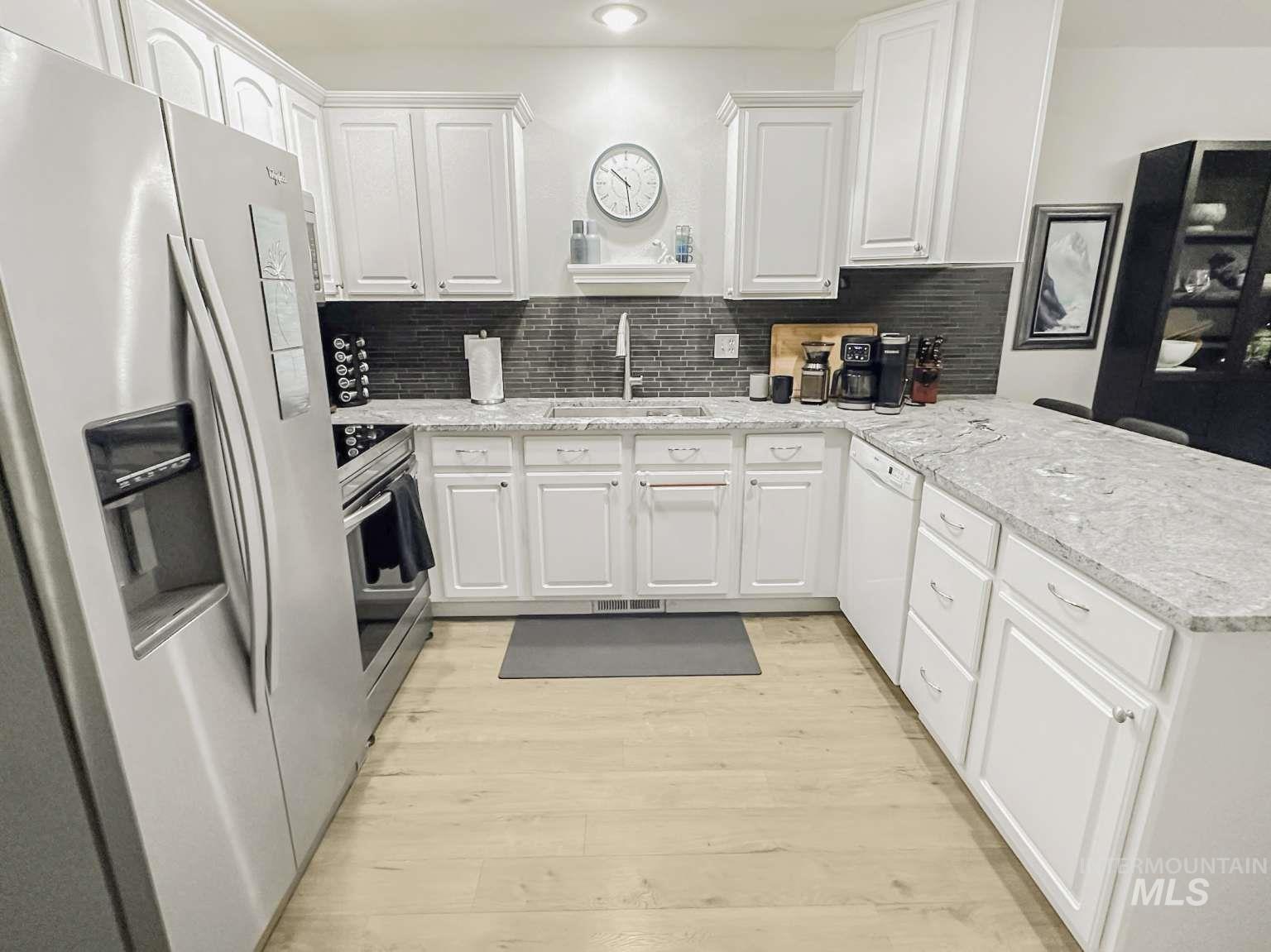Kitchen with stainless steel appliances, a peninsula, decorative backsplash, white cabinetry, and light wood finished floors
