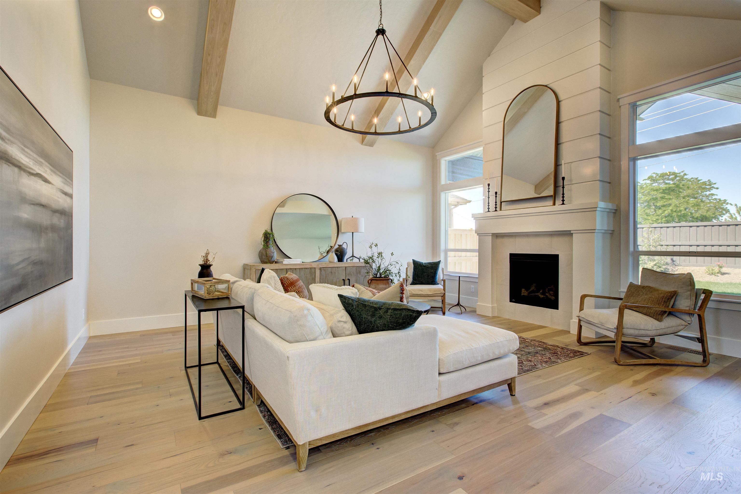 Living room with high vaulted ceiling, beam ceiling, a chandelier, light wood-style floors, and a tiled fireplace