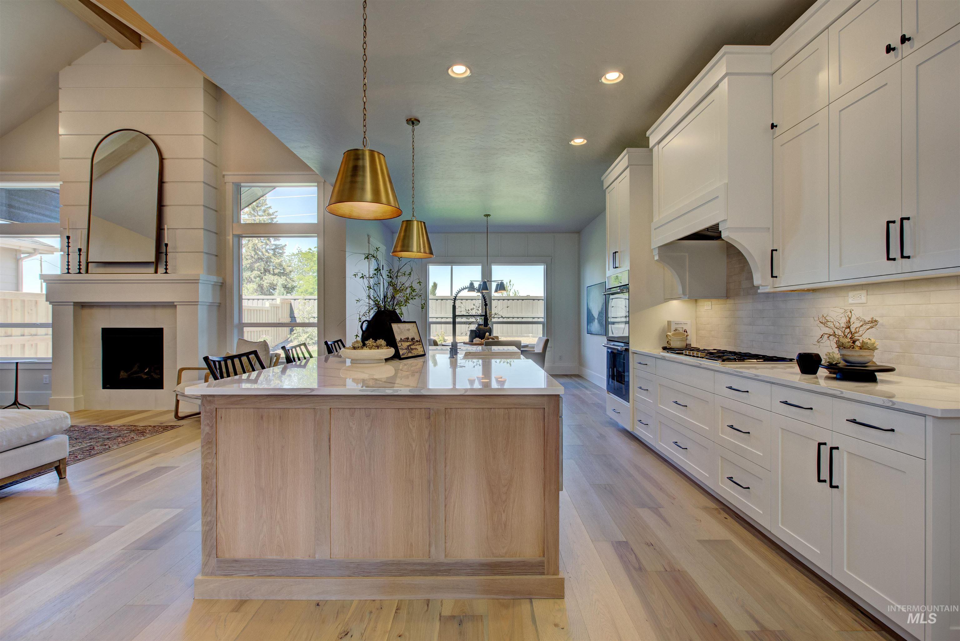 Kitchen featuring recessed lighting, light wood-type flooring, decorative backsplash, an island with sink, and a fireplace
