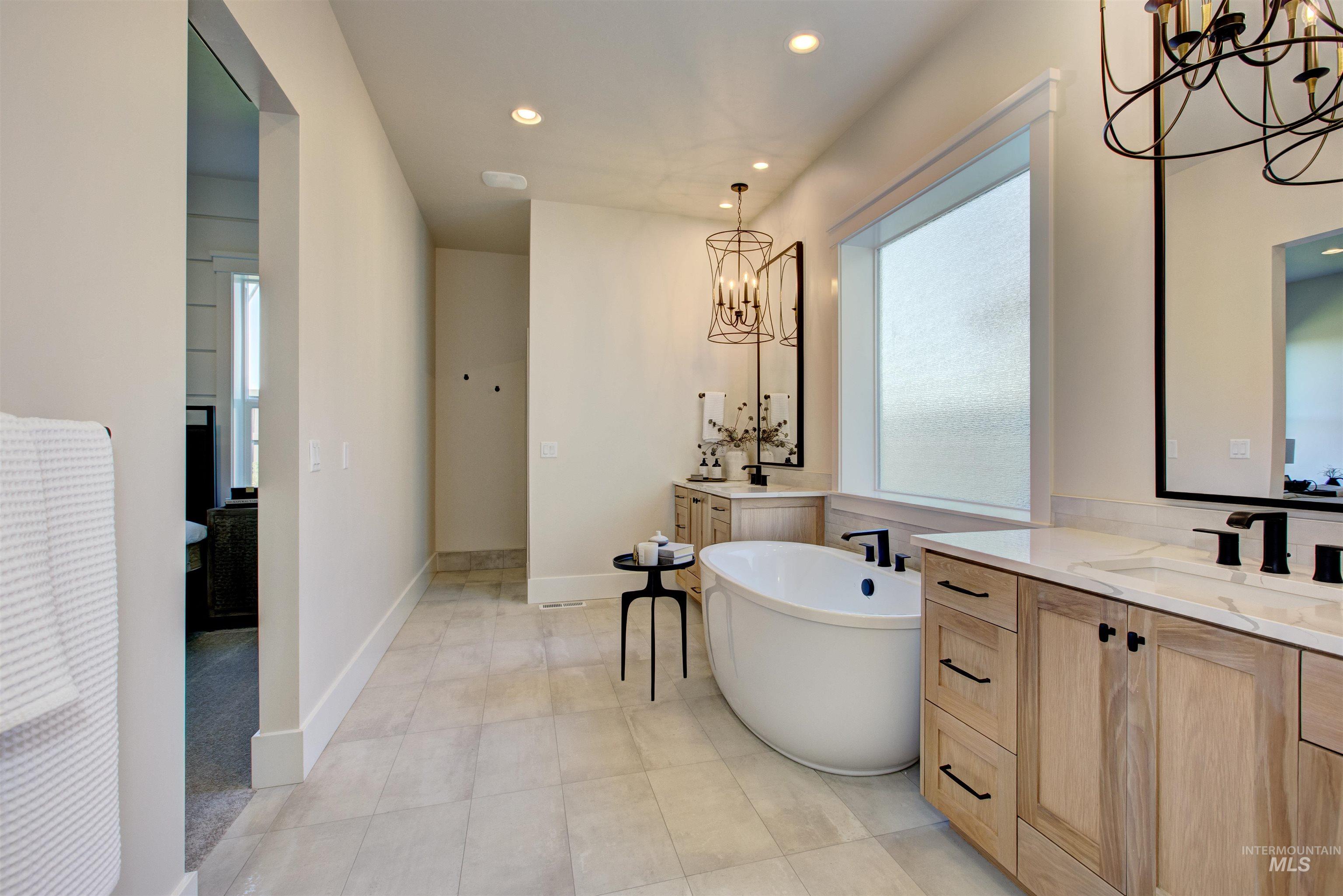 Full bathroom with a chandelier, two vanities, a freestanding bath, and recessed lighting