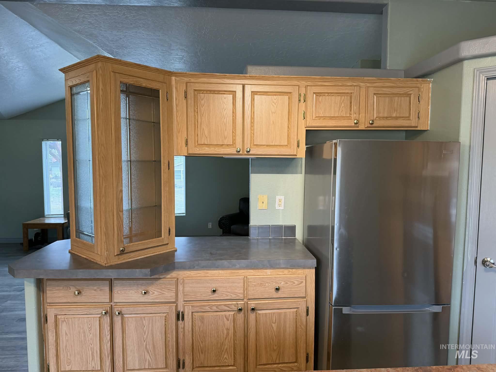 Kitchen with freestanding refrigerator, glass insert cabinets, and vaulted ceiling