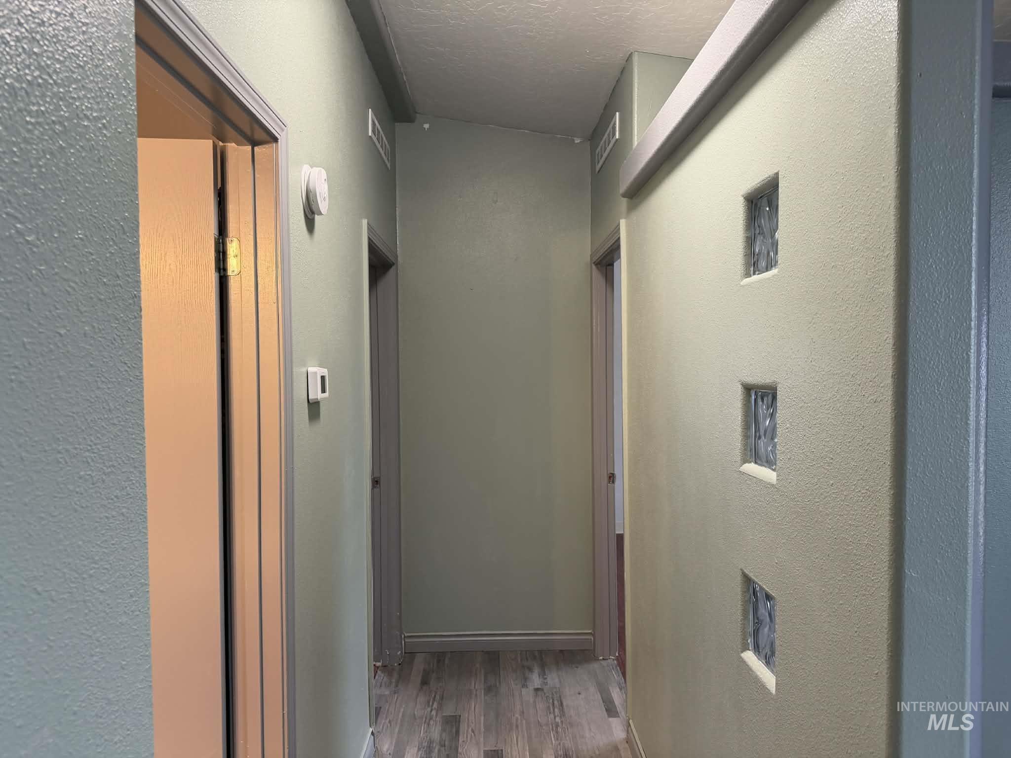 Corridor featuring a textured wall, dark wood-type flooring, and a textured ceiling