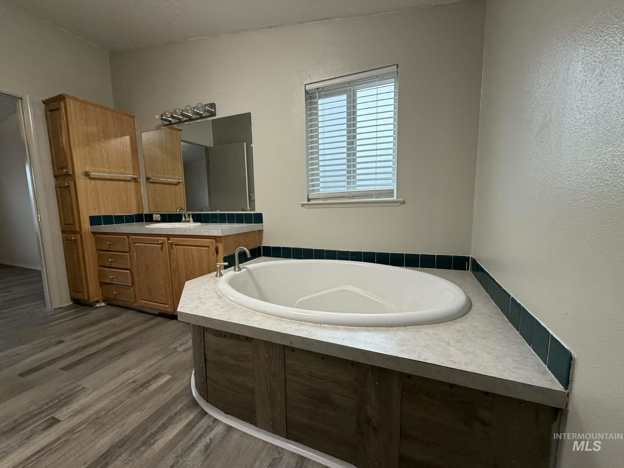 Full bath with a garden tub, vanity, dark wood-type flooring, and a textured wall