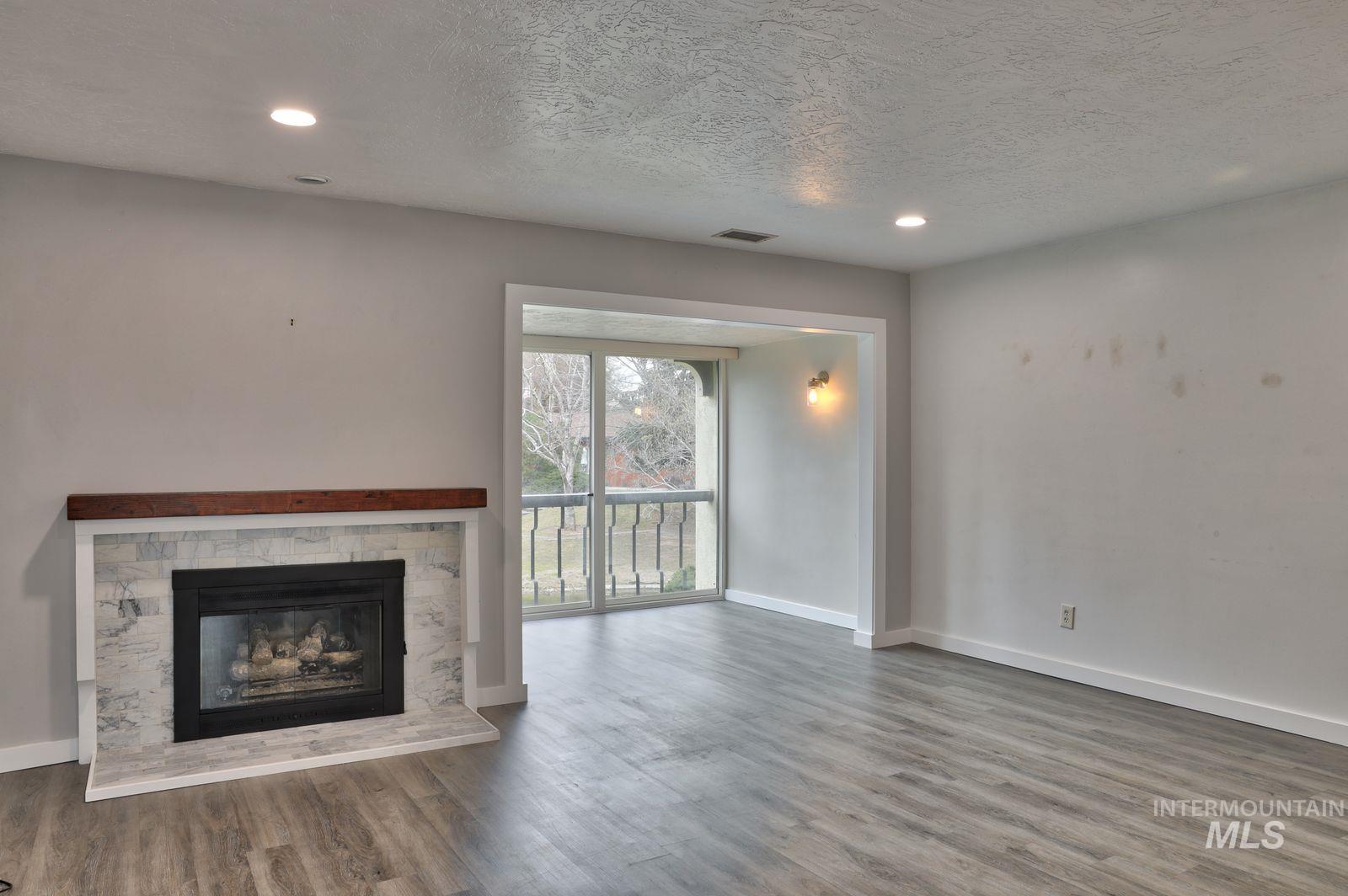 Unfurnished living room featuring a textured ceiling, a stone fireplace, recessed lighting, and dark wood-type flooring