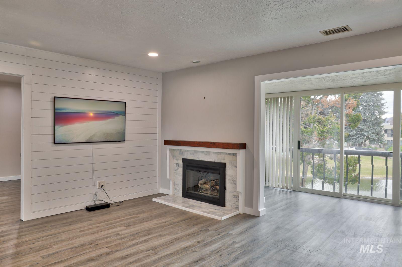 Unfurnished living room with a fireplace with raised hearth, wood finished floors, a textured ceiling, recessed lighting, and wooden walls