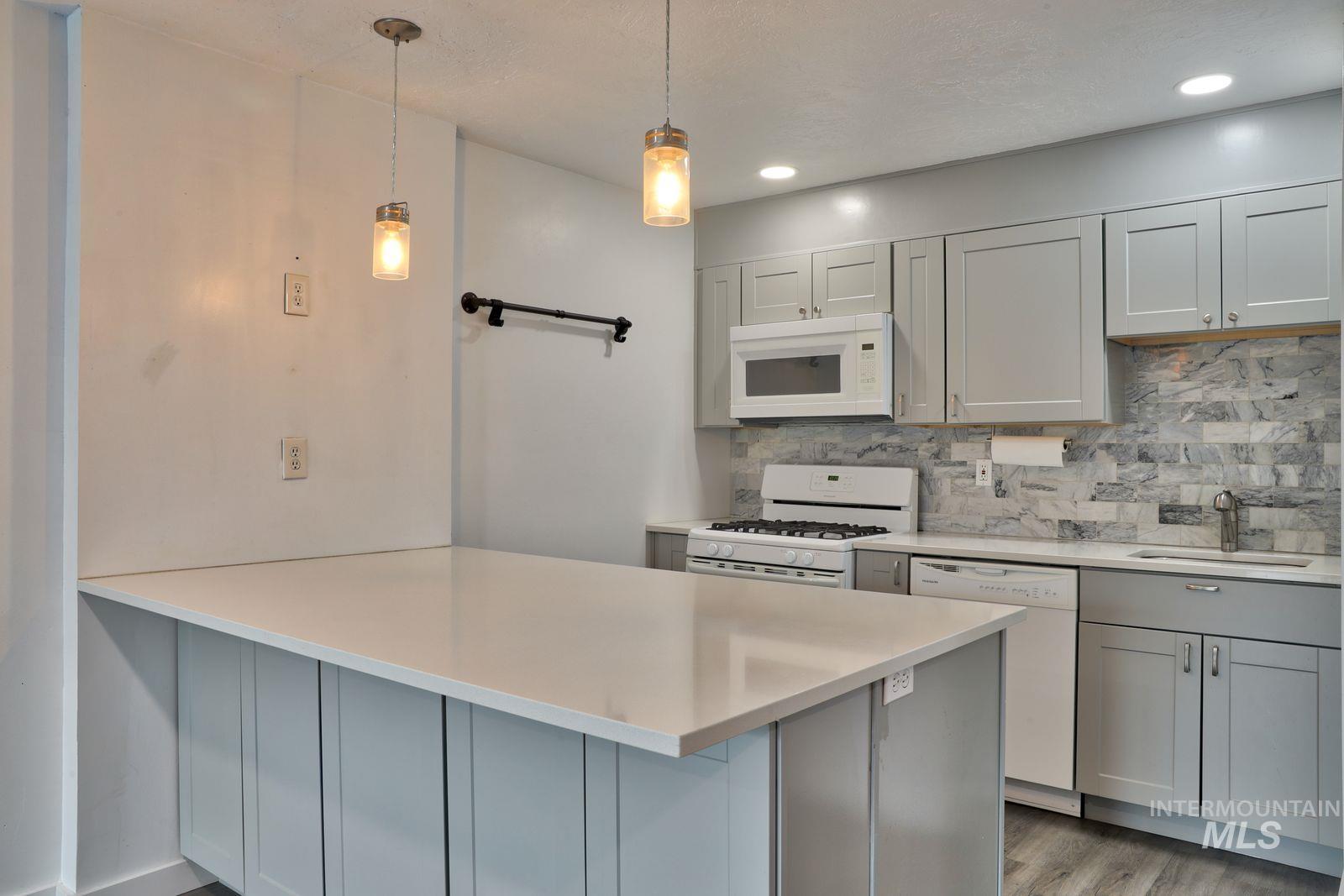 Kitchen with gray cabinetry, a peninsula, white appliances, and pendant lighting