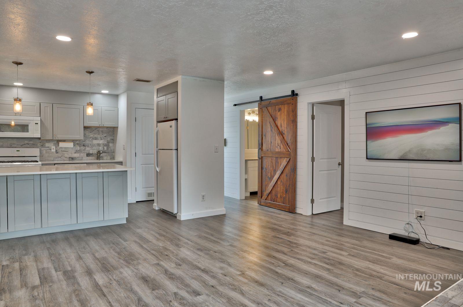 Kitchen featuring a barn door, pendant lighting, white appliances, light wood-style floors, and a textured ceiling