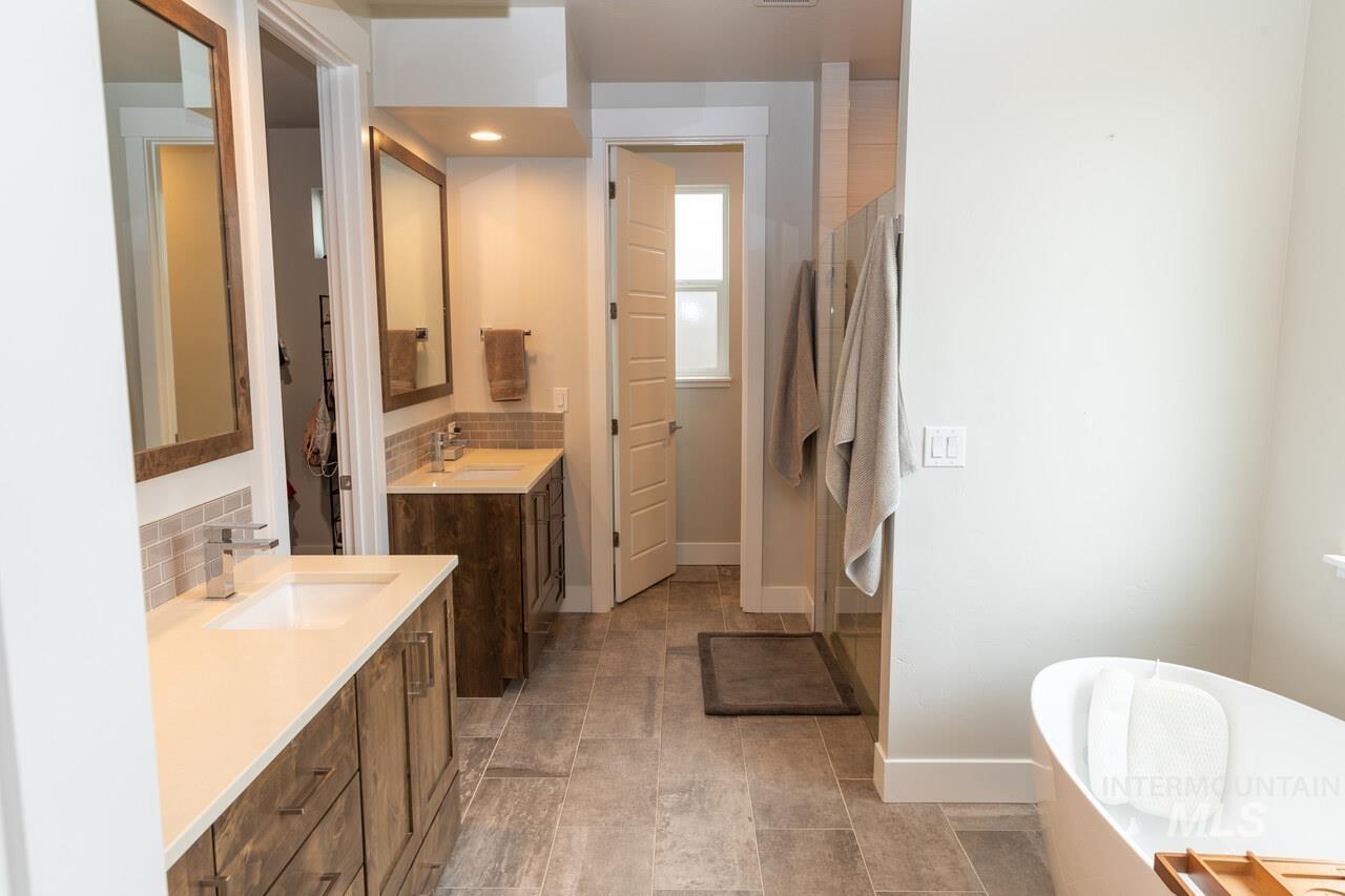 Bathroom featuring decorative backsplash, two vanities, a freestanding bath, and a stall shower