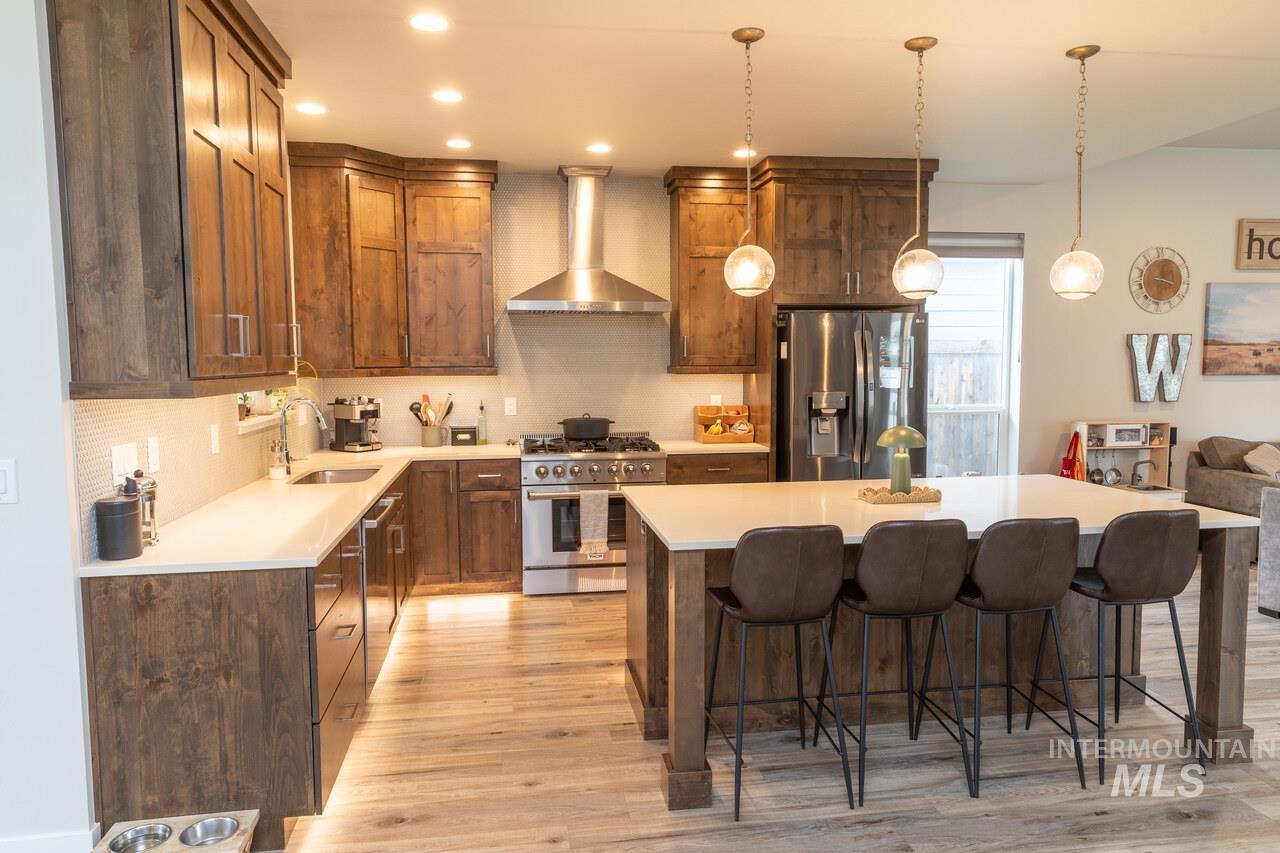 Kitchen featuring appliances with stainless steel finishes, wall chimney range hood, a kitchen island, tasteful backsplash, and pendant lighting