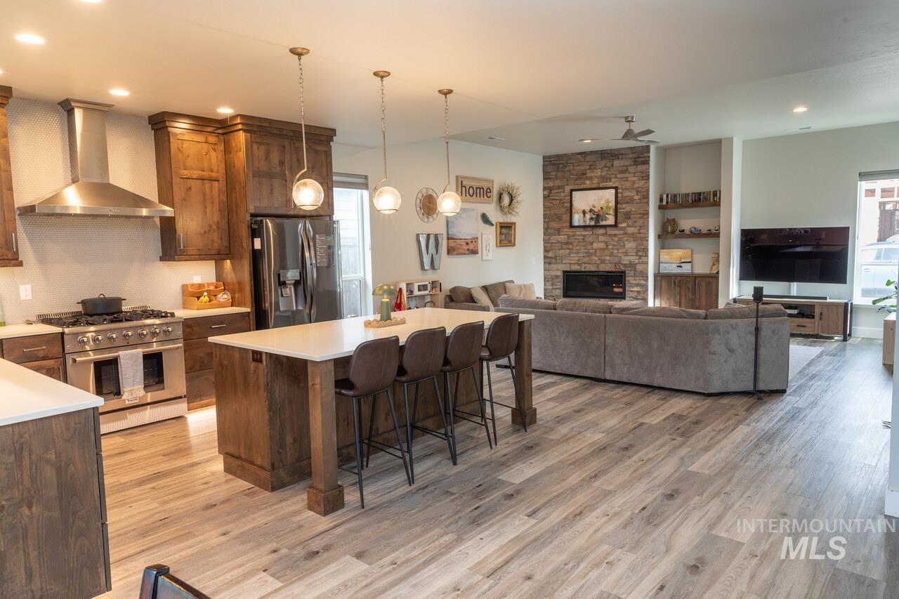 Kitchen with stainless steel appliances, wall chimney range hood, pendant lighting, a center island, and a kitchen bar
