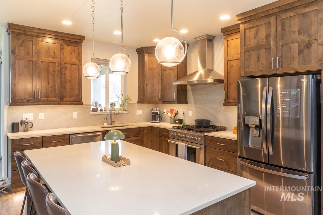 Kitchen featuring stainless steel appliances, wall chimney exhaust hood, decorative light fixtures, a center island, and backsplash