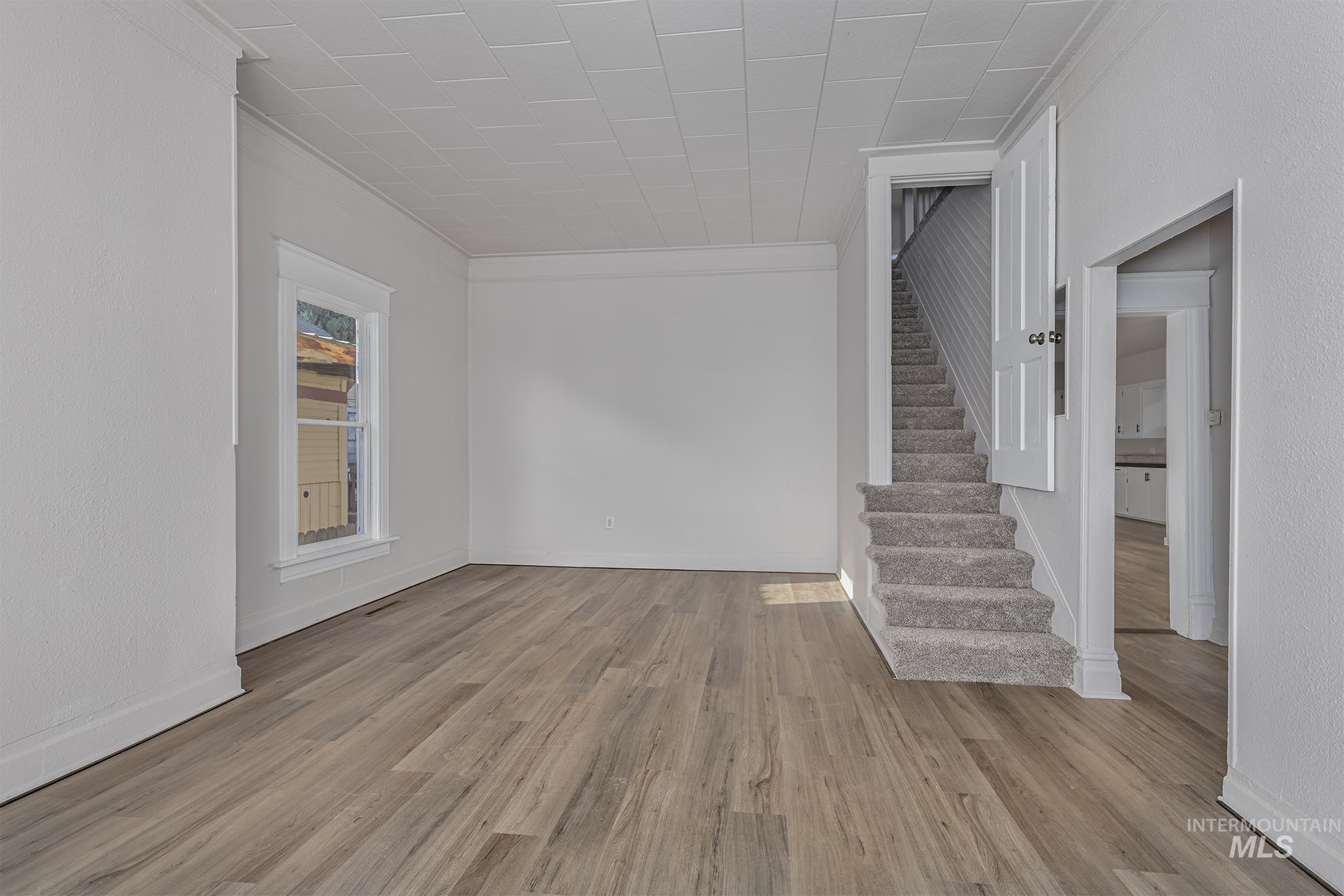 Unfurnished room featuring stairs, wood finished floors, and ornamental molding