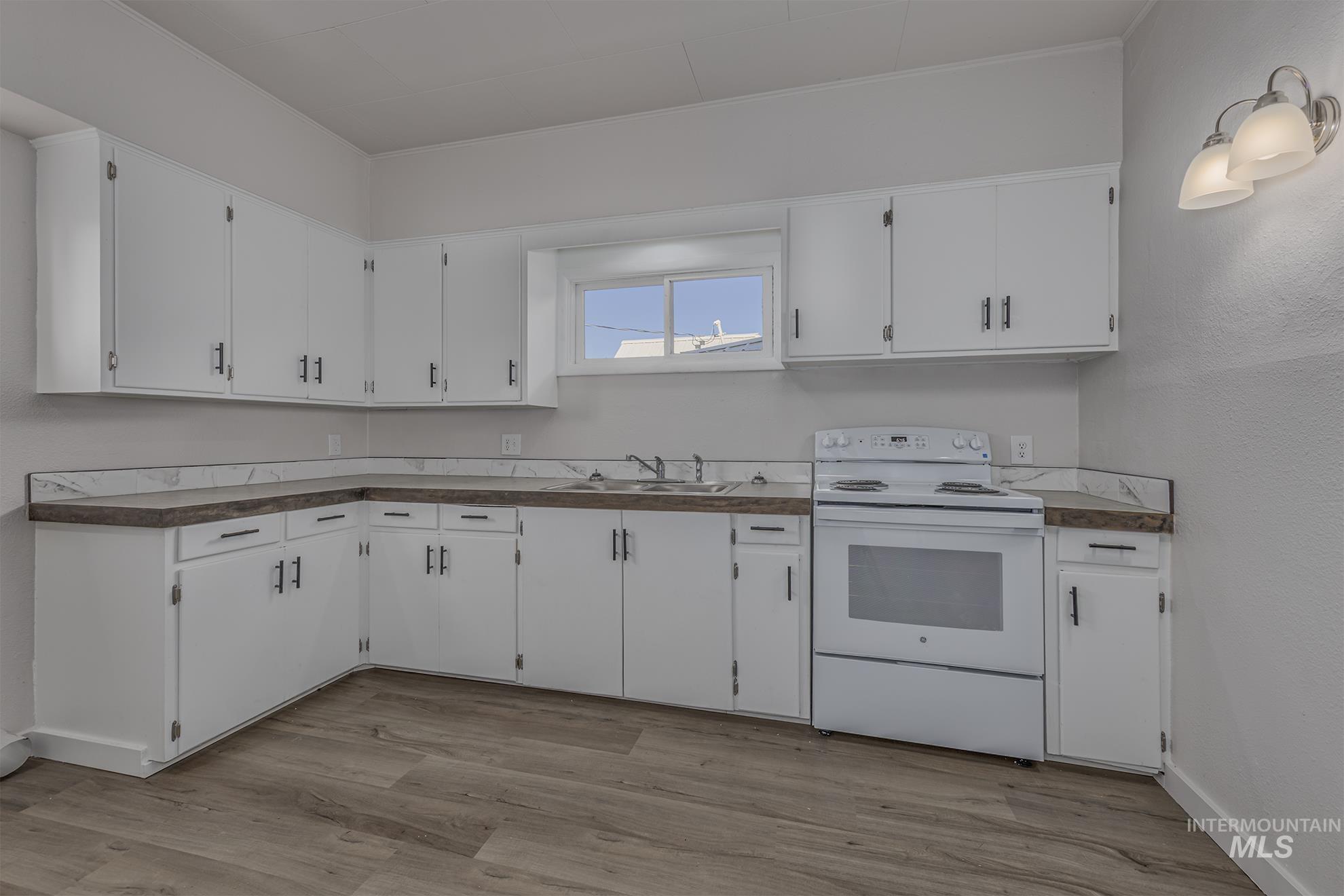 Kitchen with white range with electric stovetop, white cabinets, wood finished floors