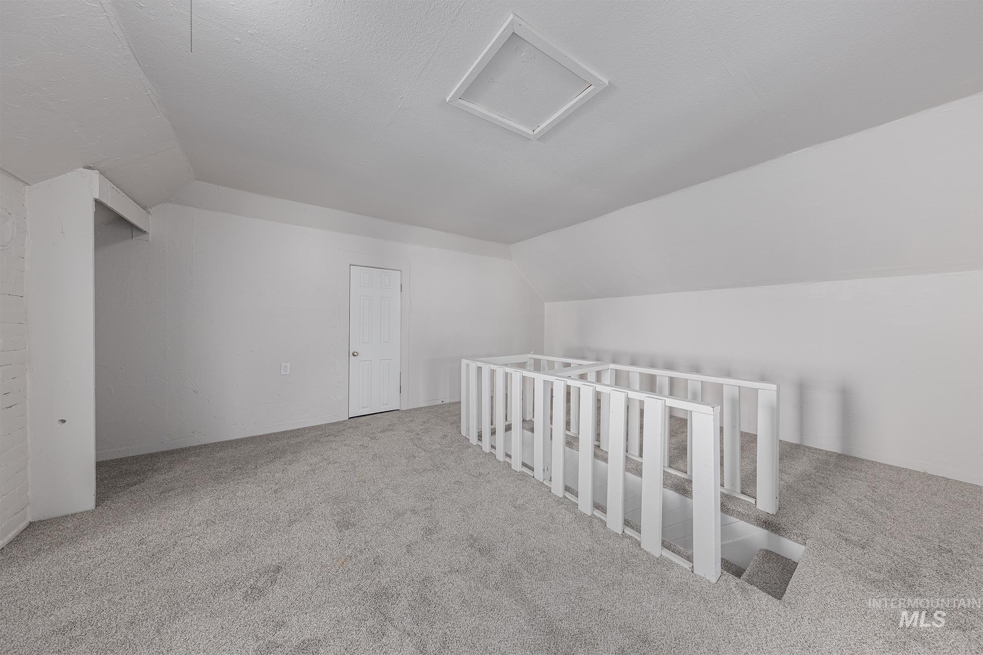 Additional living space with vaulted ceiling, carpet flooring, and attic access