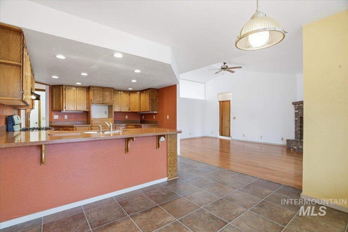Kitchen with a kitchen breakfast bar, brown cabinets, pendant lighting, lofted ceiling, and a peninsula
