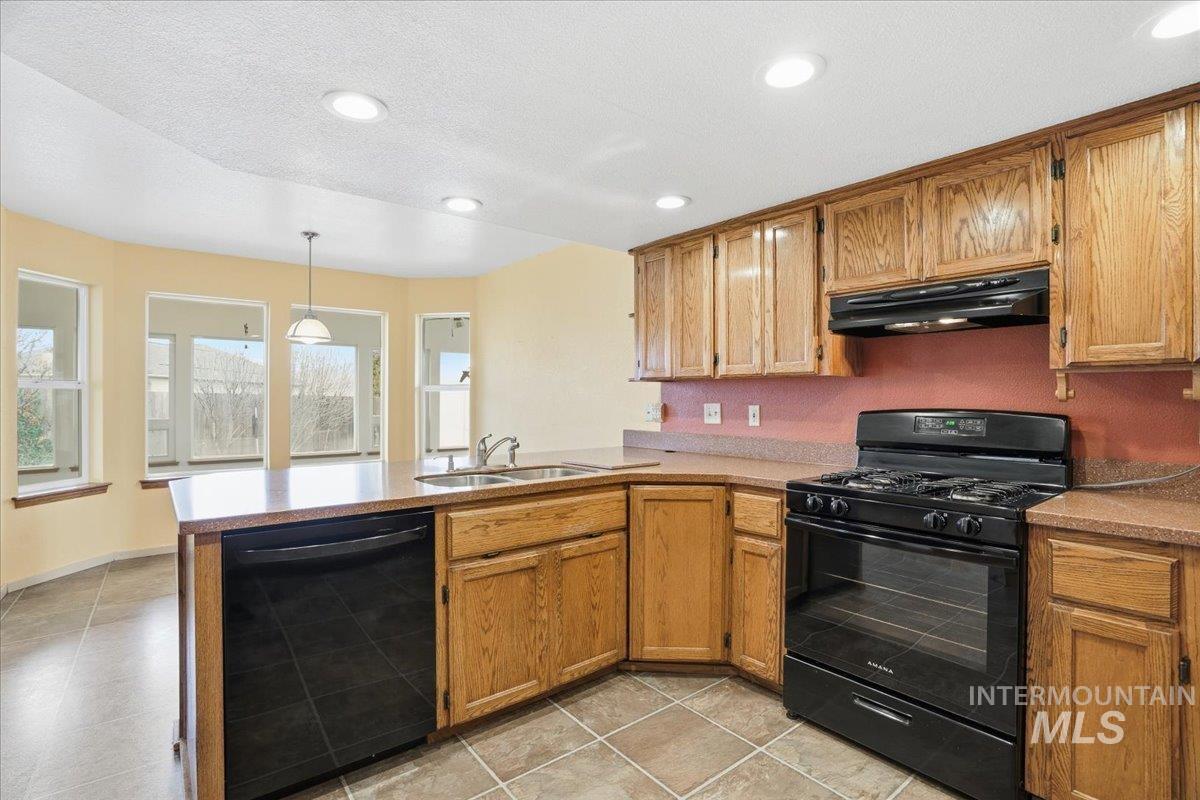 Kitchen with black appliances, a peninsula, hanging light fixtures, under cabinet range hood, and brown cabinets