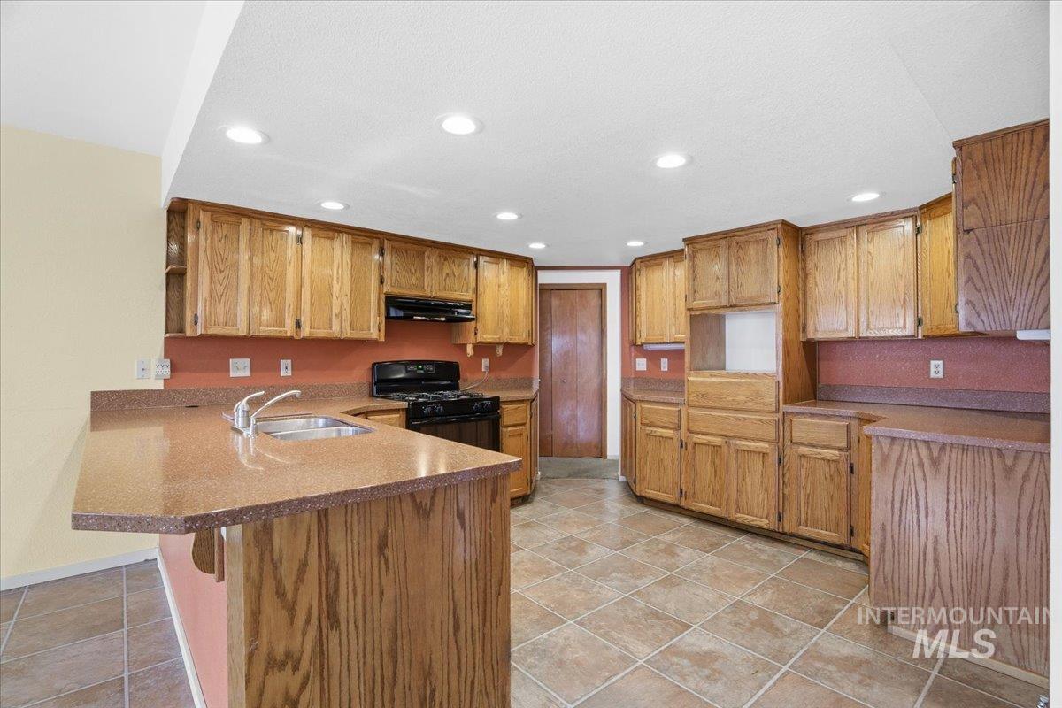 Kitchen featuring black gas range oven, a peninsula, a kitchen breakfast bar, brown cabinetry, and recessed lighting