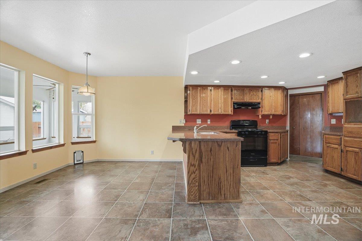 Kitchen with a kitchen breakfast bar, brown cabinets, black range with gas stovetop, a peninsula, and hanging light fixtures