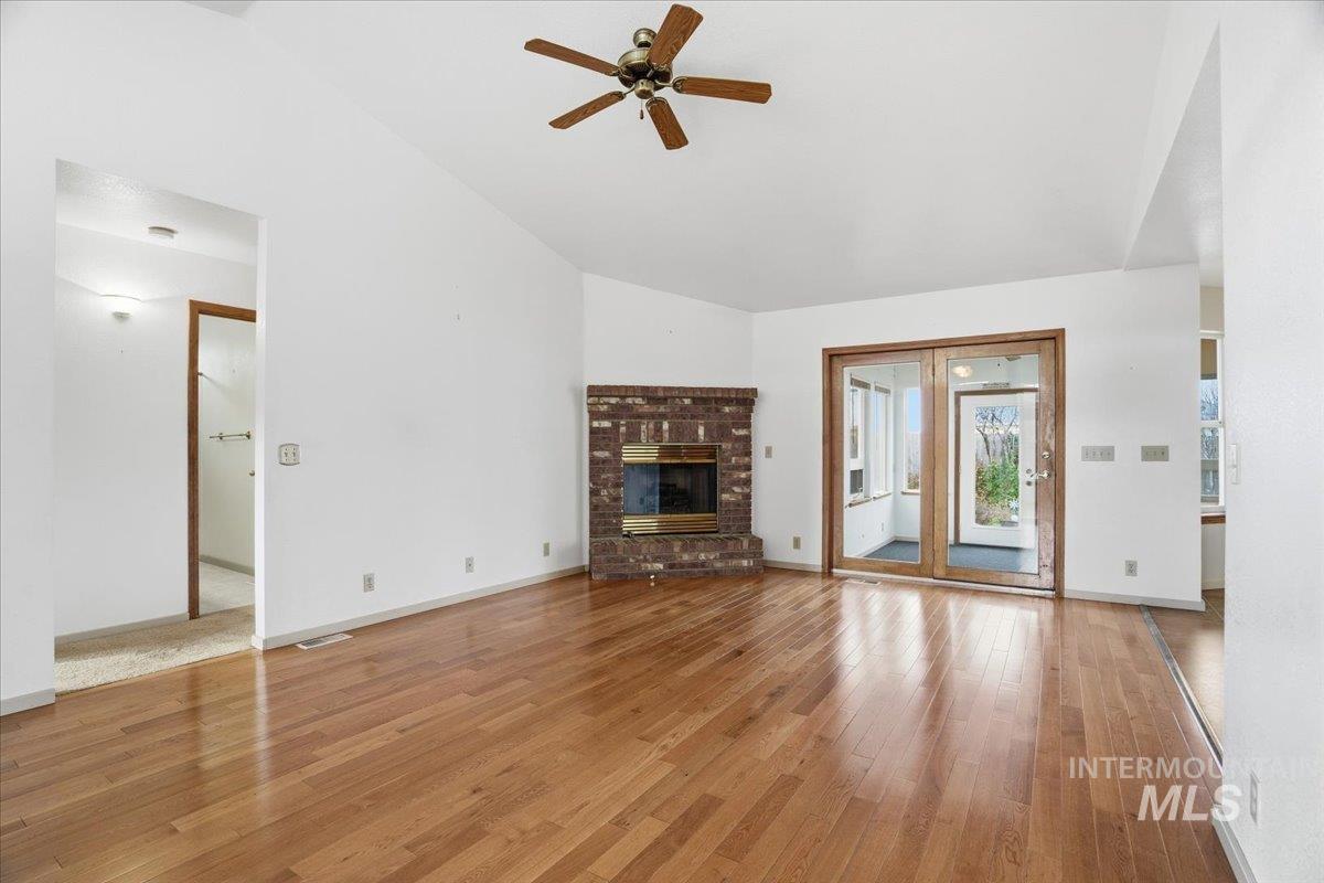 Unfurnished living room with vaulted ceiling, a brick fireplace, light wood finished floors, and a ceiling fan