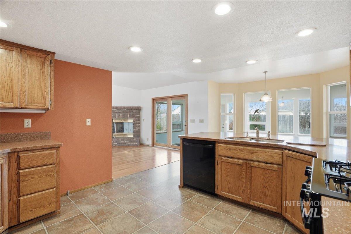 Kitchen with gas range, dishwasher, brown cabinets, hanging light fixtures, and plenty of natural light