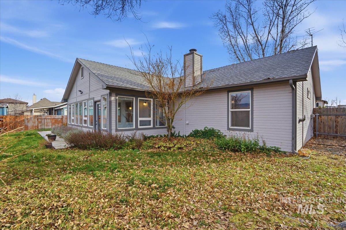 Rear view of house featuring a sunroom, roof with shingles, and a chimney