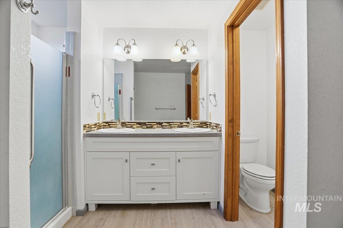 Bathroom with double vanity, a stall shower, and light wood-style floors
