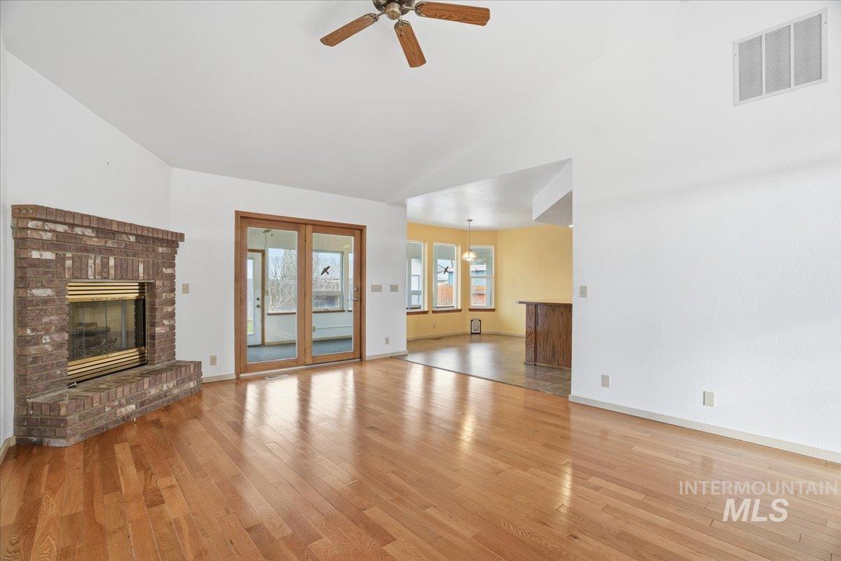 Unfurnished living room featuring a brick fireplace, light wood-style flooring, and ceiling fan