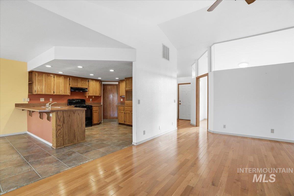 Kitchen featuring light wood-type flooring, brown cabinets, black gas range oven, open shelves, and a kitchen bar