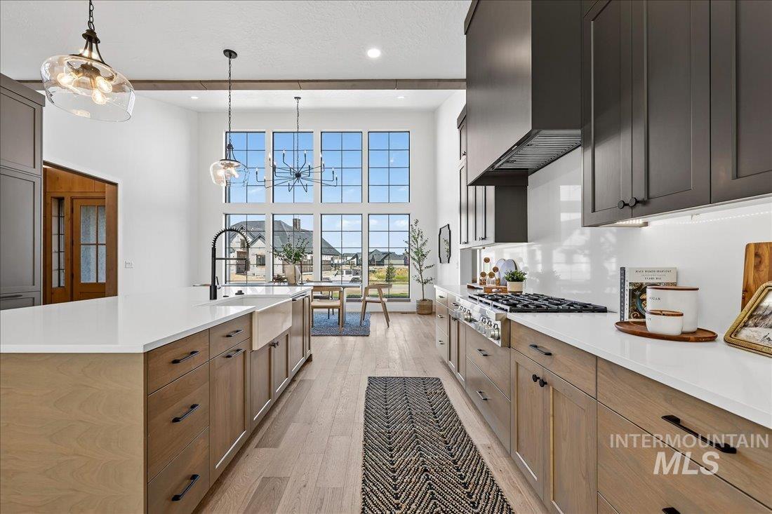 Kitchen featuring light wood finished floors, a chandelier, a towering ceiling, pendant lighting, and light stone countertops