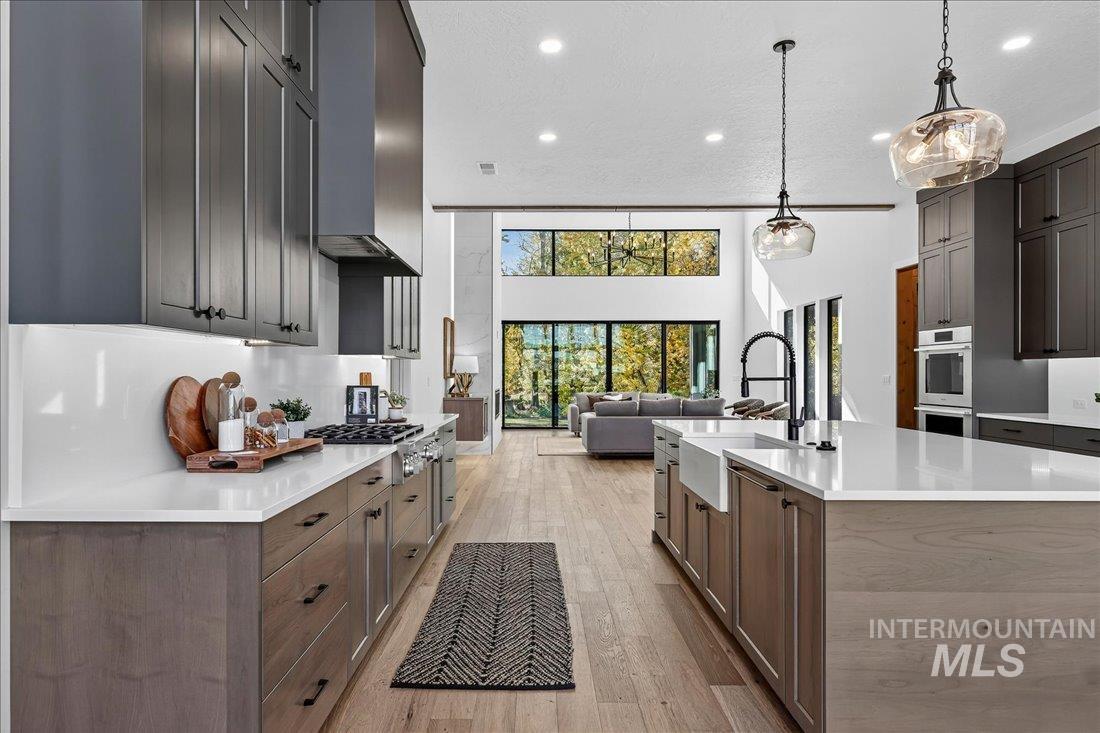 Kitchen with light wood-style floors, open floor plan, recessed lighting, a kitchen island with sink, and decorative light fixtures