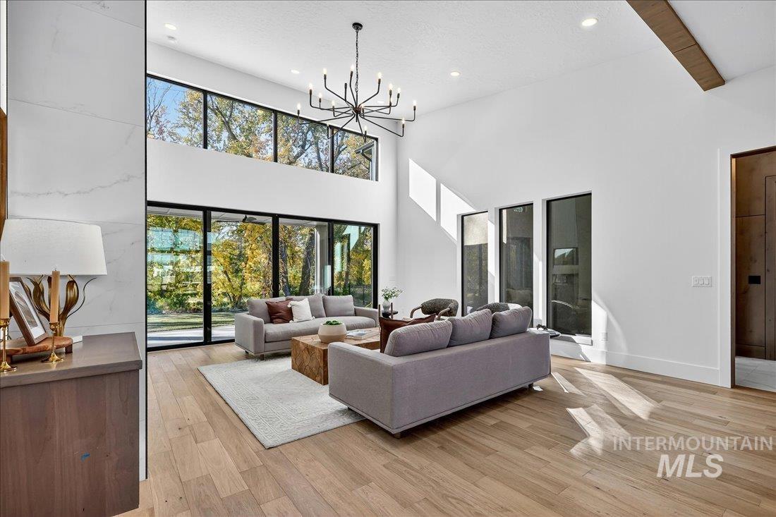 Living room featuring light wood-style floors, recessed lighting, a chandelier, a towering ceiling, and beamed ceiling