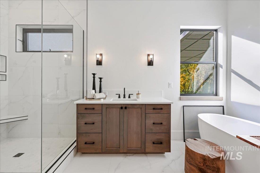 Bathroom featuring plenty of natural light, vanity, light marble finish floors, and a marble finish shower