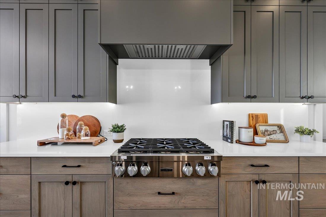 Kitchen featuring under cabinet range hood, stainless steel gas cooktop, and light stone counters
