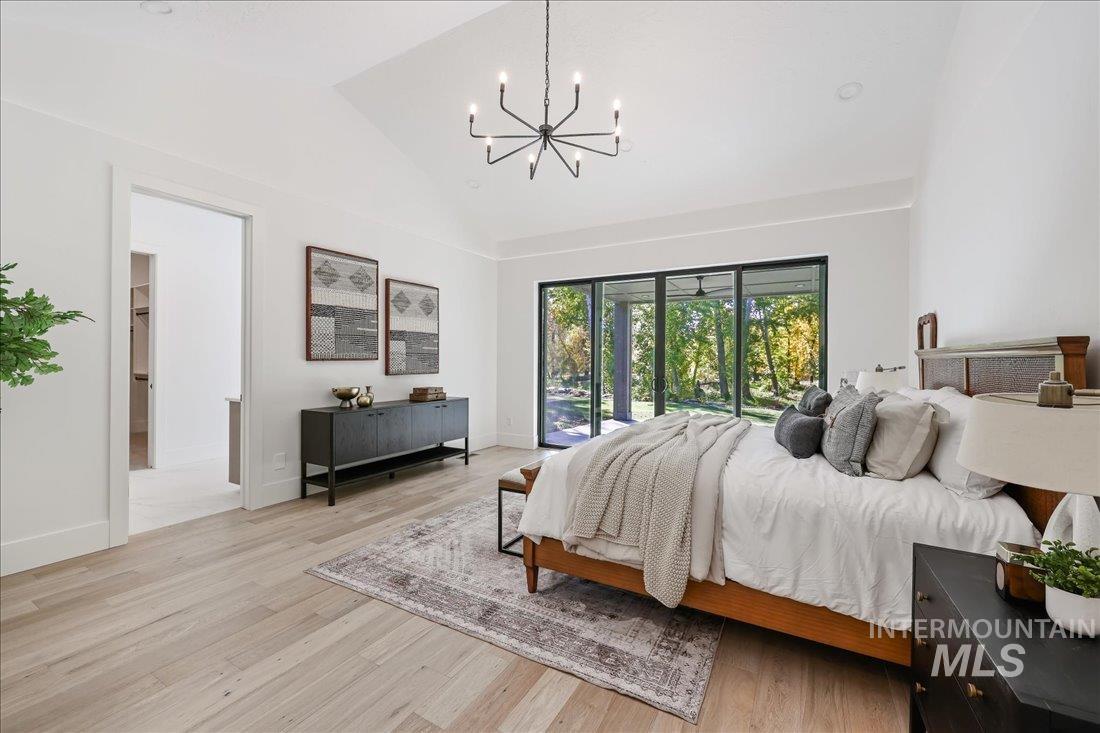 Bedroom with light wood finished floors, a chandelier, lofted ceiling, and access to exterior