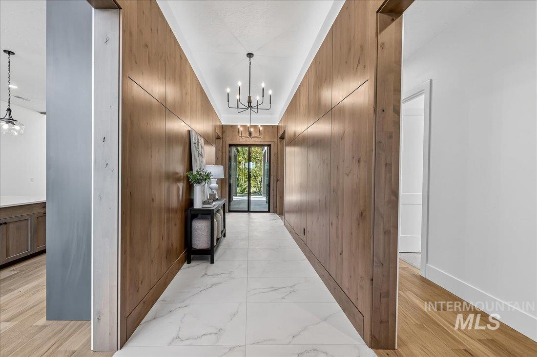 Hall with a chandelier, light marble finish floors, and wooden walls