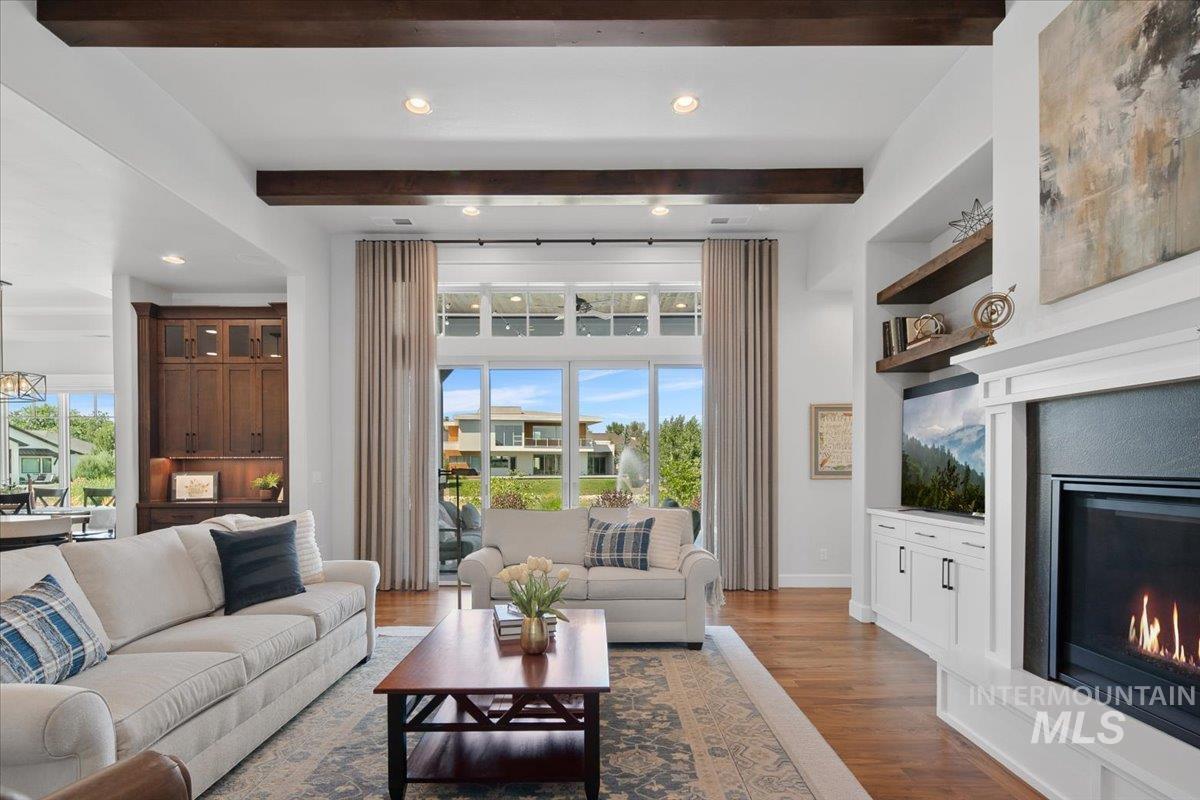 Living room featuring a glass covered fireplace, healthy amount of natural light, wood finished floors, beamed ceiling, and recessed lighting