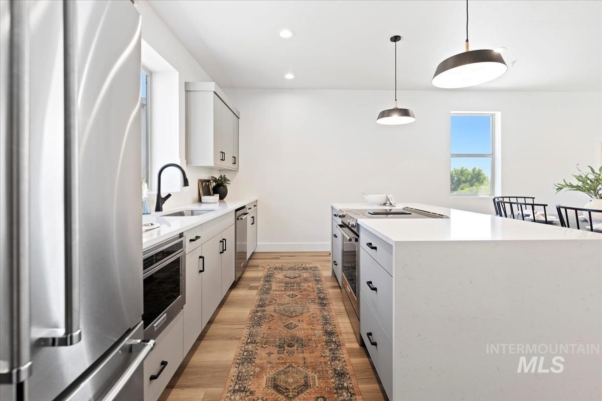 Kitchen with appliances with stainless steel finishes, light stone counters, hanging light fixtures, white cabinetry, and recessed lighting