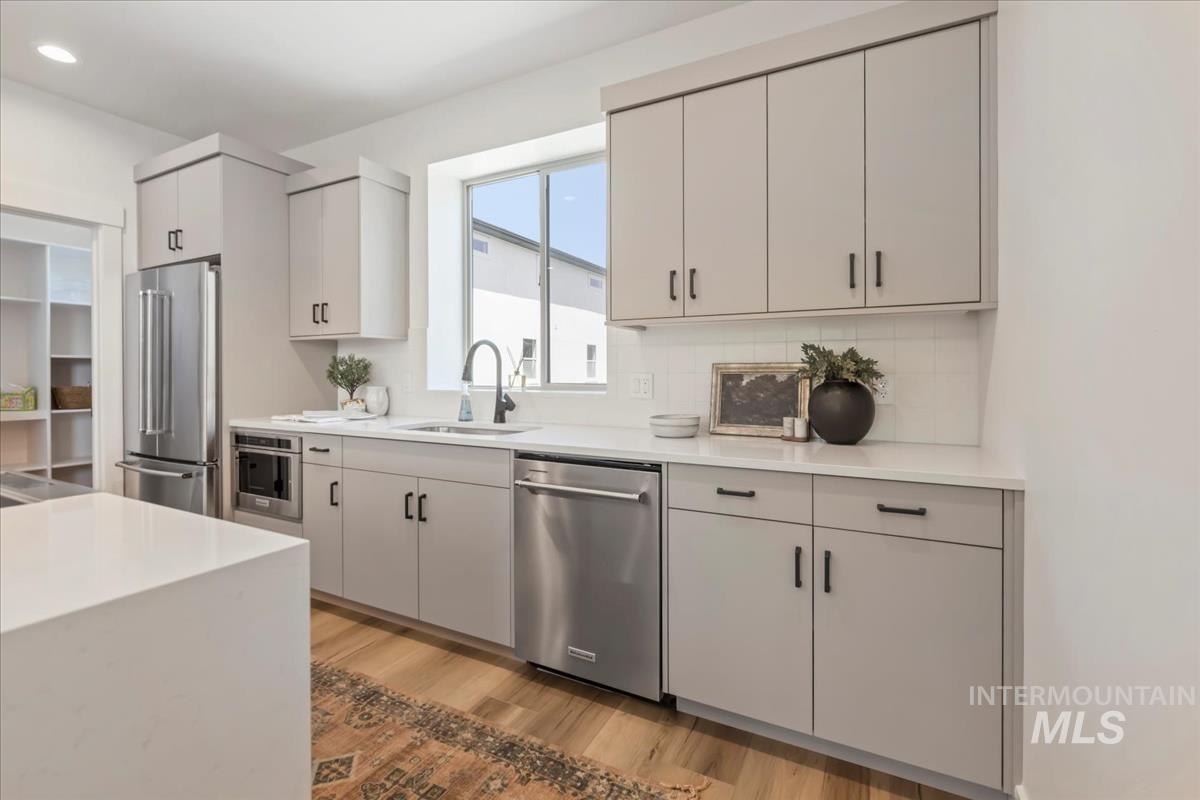Kitchen featuring stainless steel appliances, light wood finished floors, light stone counters, decorative backsplash, and white cabinets