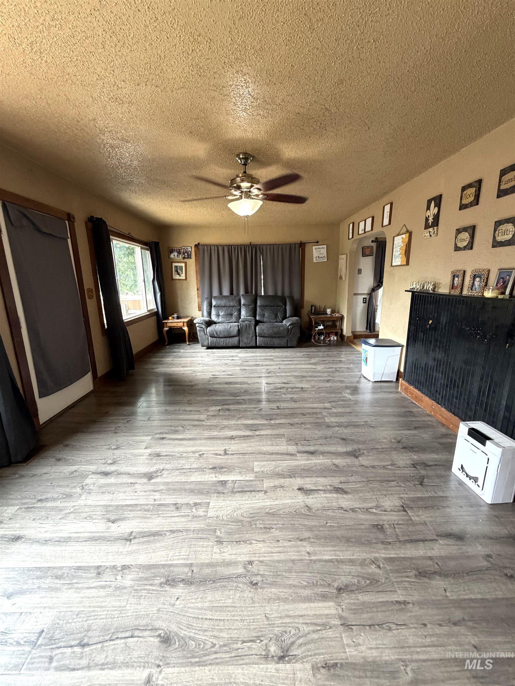 Spacious interior featuring wood-finish flooring, a ceiling fan with integrated lighting, and multiple windows
