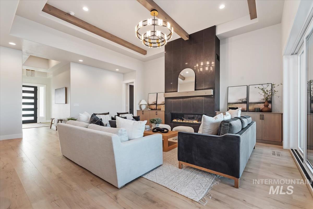 Living area with a large fireplace, a tray ceiling, light wood-style flooring, a chandelier, and recessed lighting