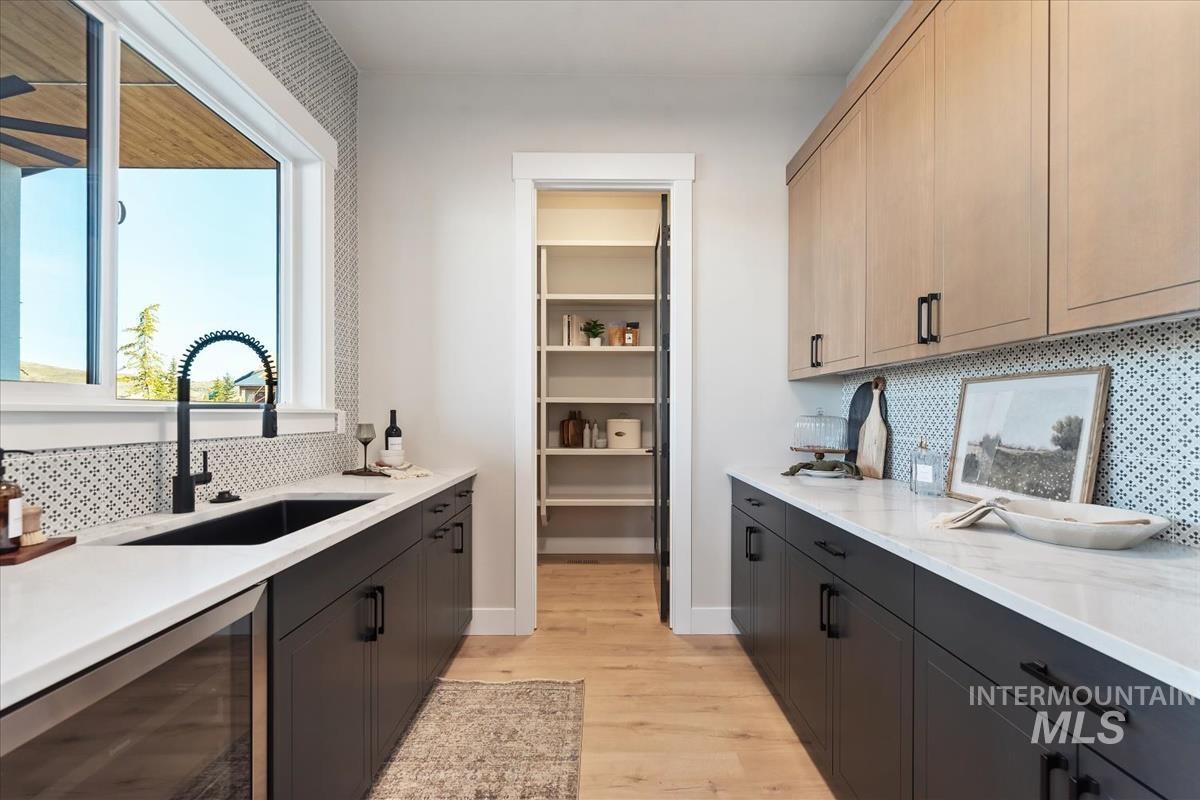 Kitchen with decorative backsplash, beverage cooler, light wood-style floors, and light stone countertops