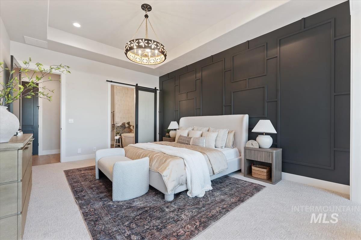 Bedroom featuring a barn door, light colored carpet, a raised ceiling, ensuite bath, and recessed lighting