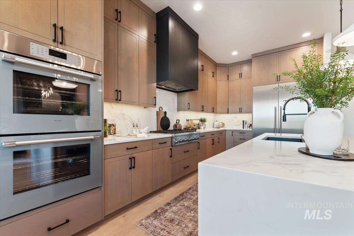 Kitchen featuring stainless steel appliances, light stone counters, pendant lighting, light wood-type flooring, and custom exhaust hood