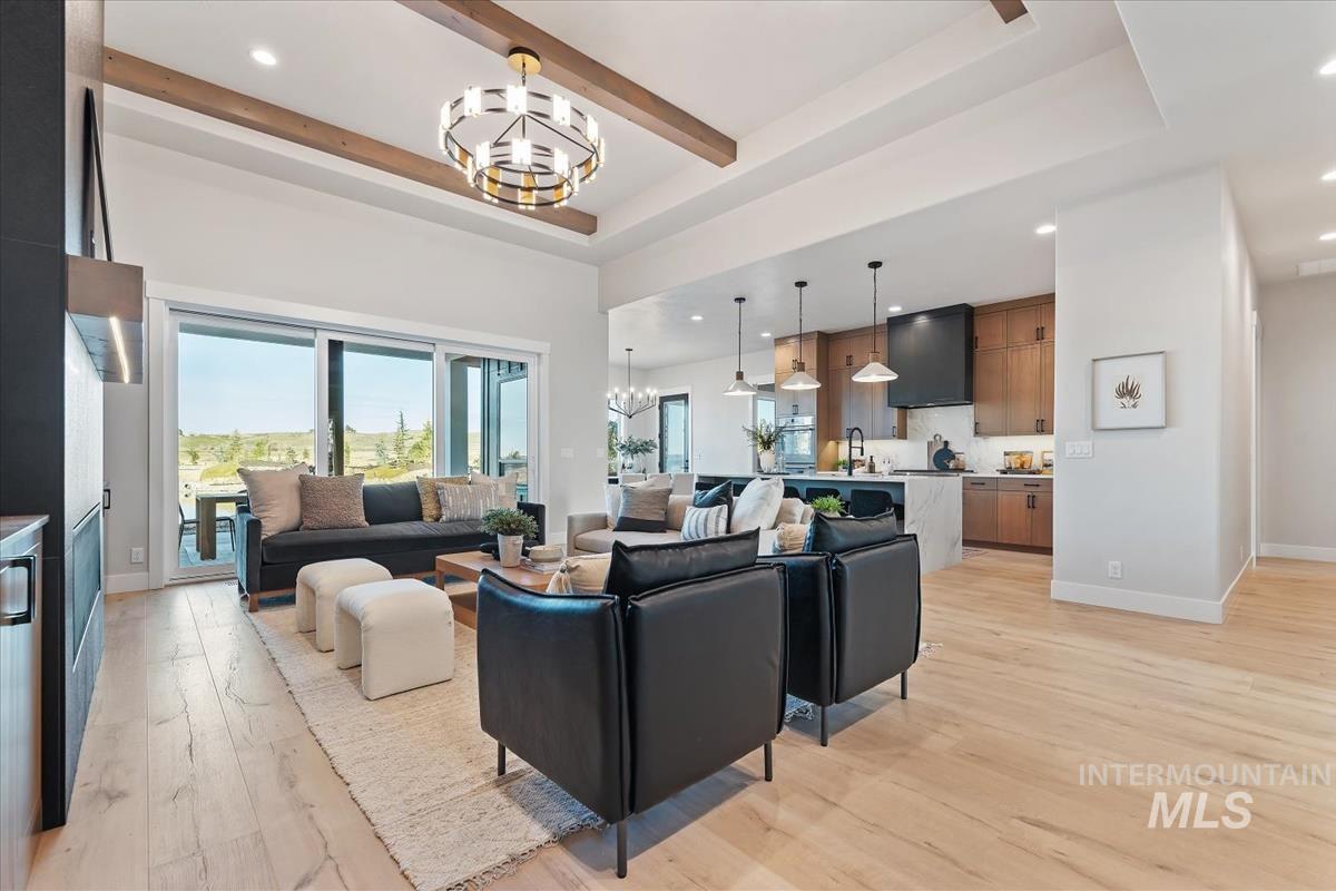 Living area with a chandelier, recessed lighting, light wood finished floors, beam ceiling, and a tray ceiling