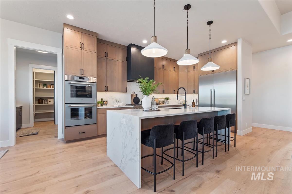 Kitchen with appliances with stainless steel finishes, a kitchen island with sink, hanging light fixtures, a kitchen breakfast bar, and light stone countertops