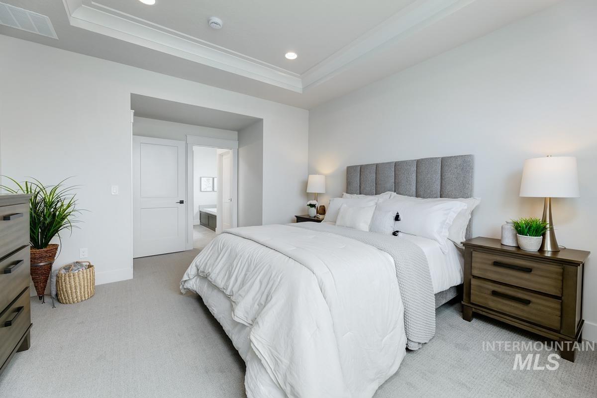 Bedroom with a raised ceiling, ensuite bathroom, light carpet, recessed lighting, and ornamental molding