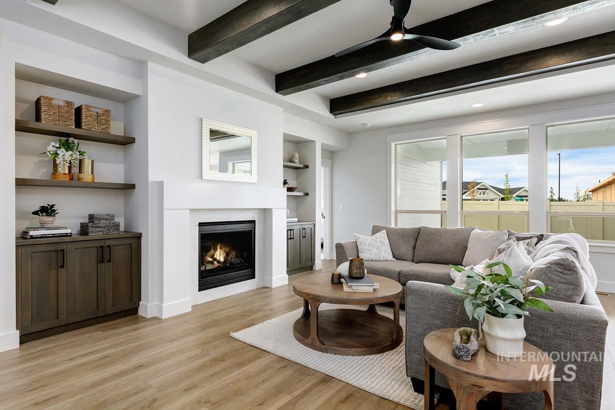 Living area featuring built in features, a glass covered fireplace, beam ceiling, light wood-style flooring, and a ceiling fan