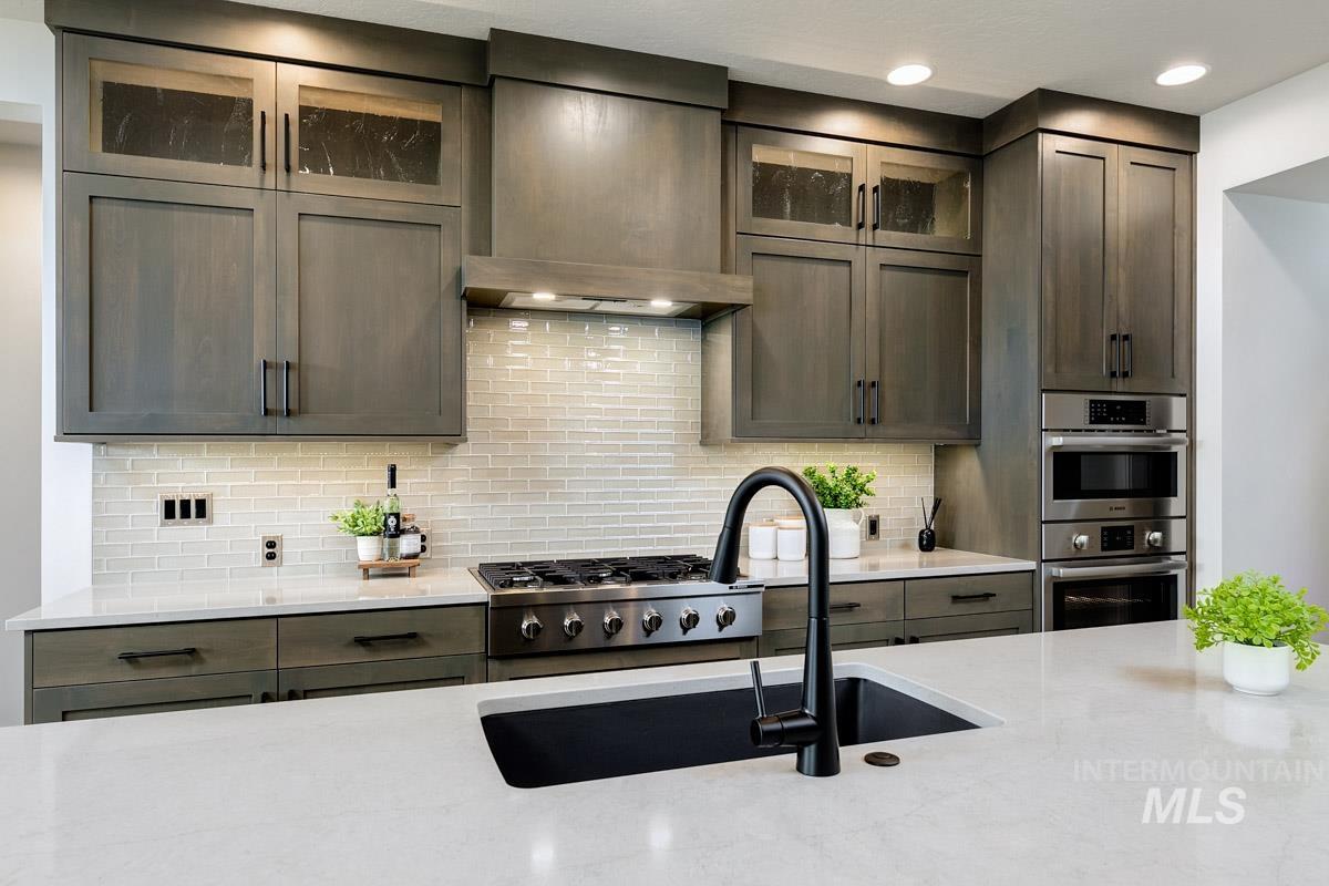 Kitchen with glass insert cabinets, custom exhaust hood, stainless steel appliances, decorative backsplash, and light stone counters